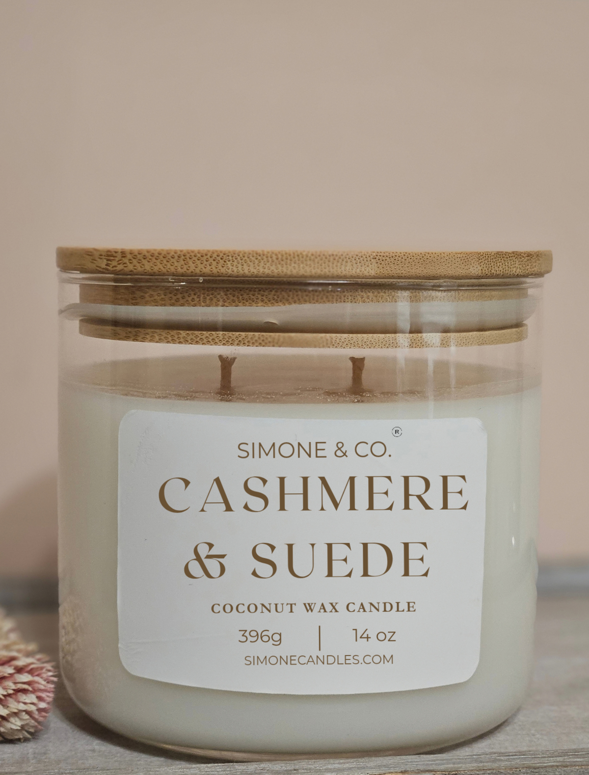 A Simone & Co. 'Cashmere & Suede' coconut wax candle in a clear glass jar with a bamboo lid, set against a soft beige background.