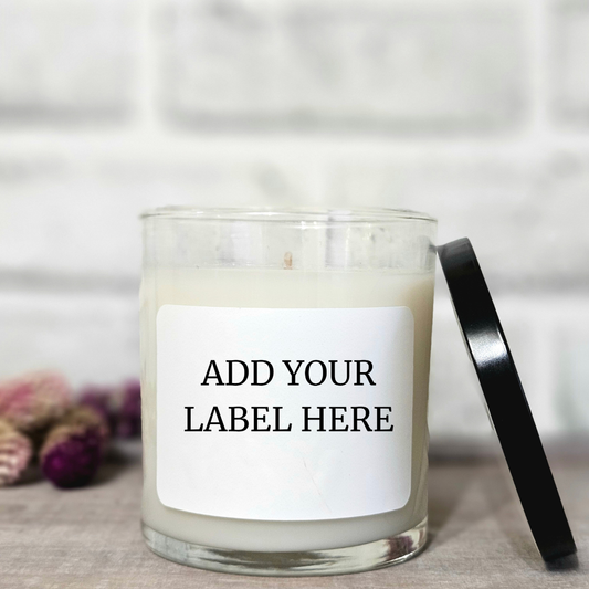 Clear glass candle with a black lid on a neutral background