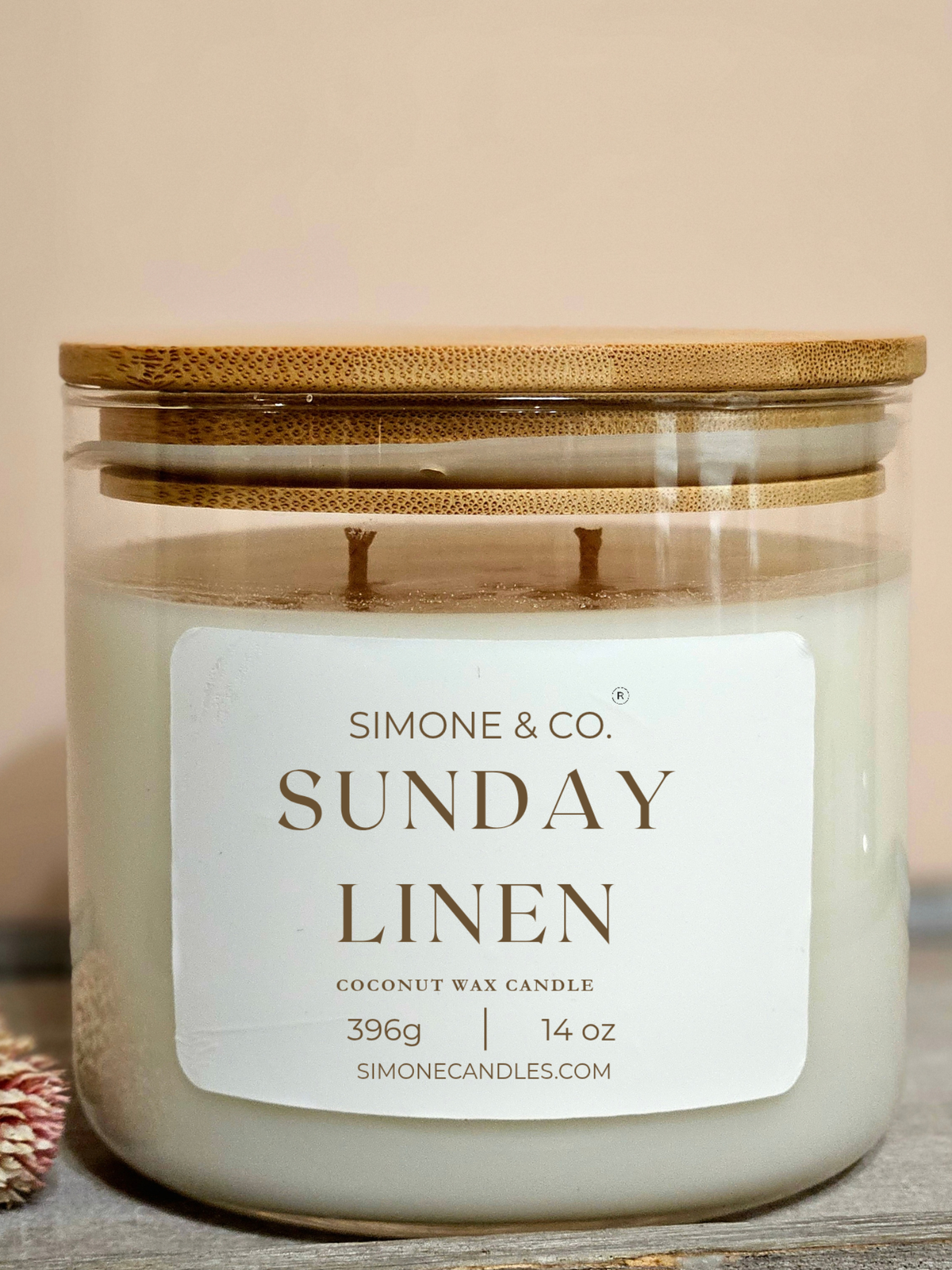 A Simone & Co. 'Sunday Linen' coconut wax candle in a clear glass jar with a bamboo lid, resting on a rustic wooden surface.